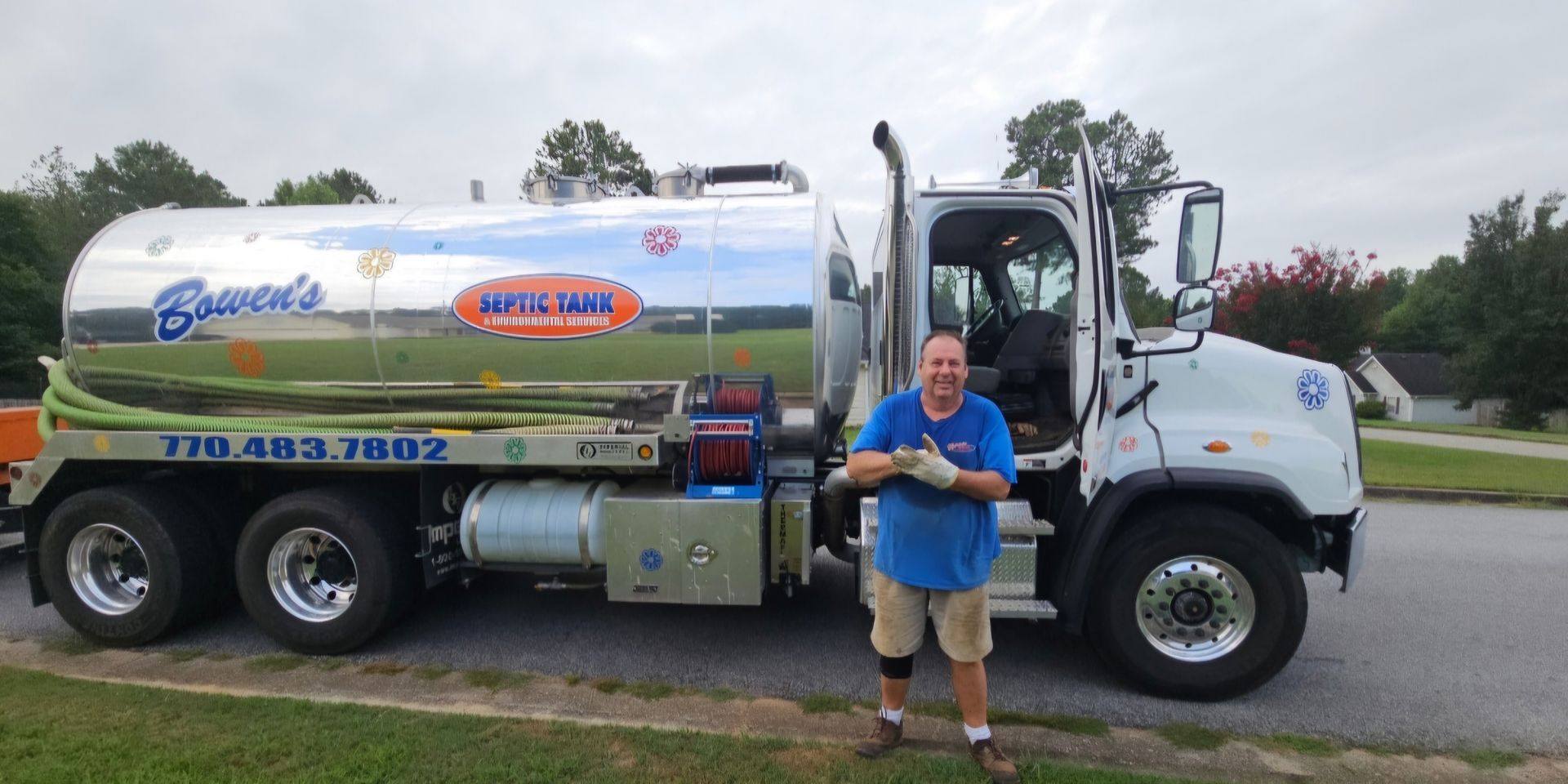 A man in a blue shirt is standing in front of a tanker truck.