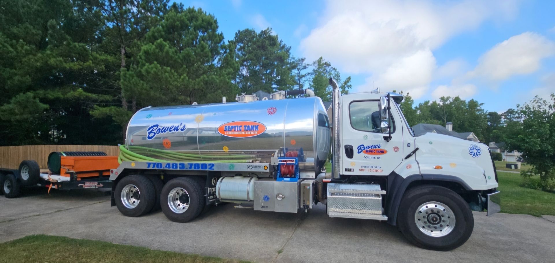 A tanker truck is parked in a driveway next to a trailer.