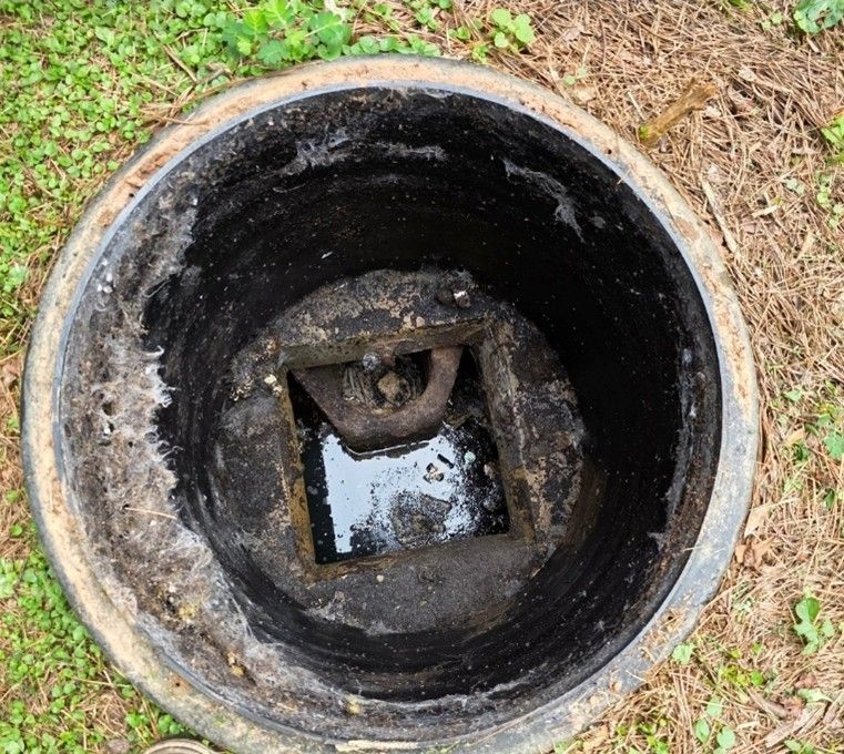 Open septic tank, black interior, murky water at bottom.