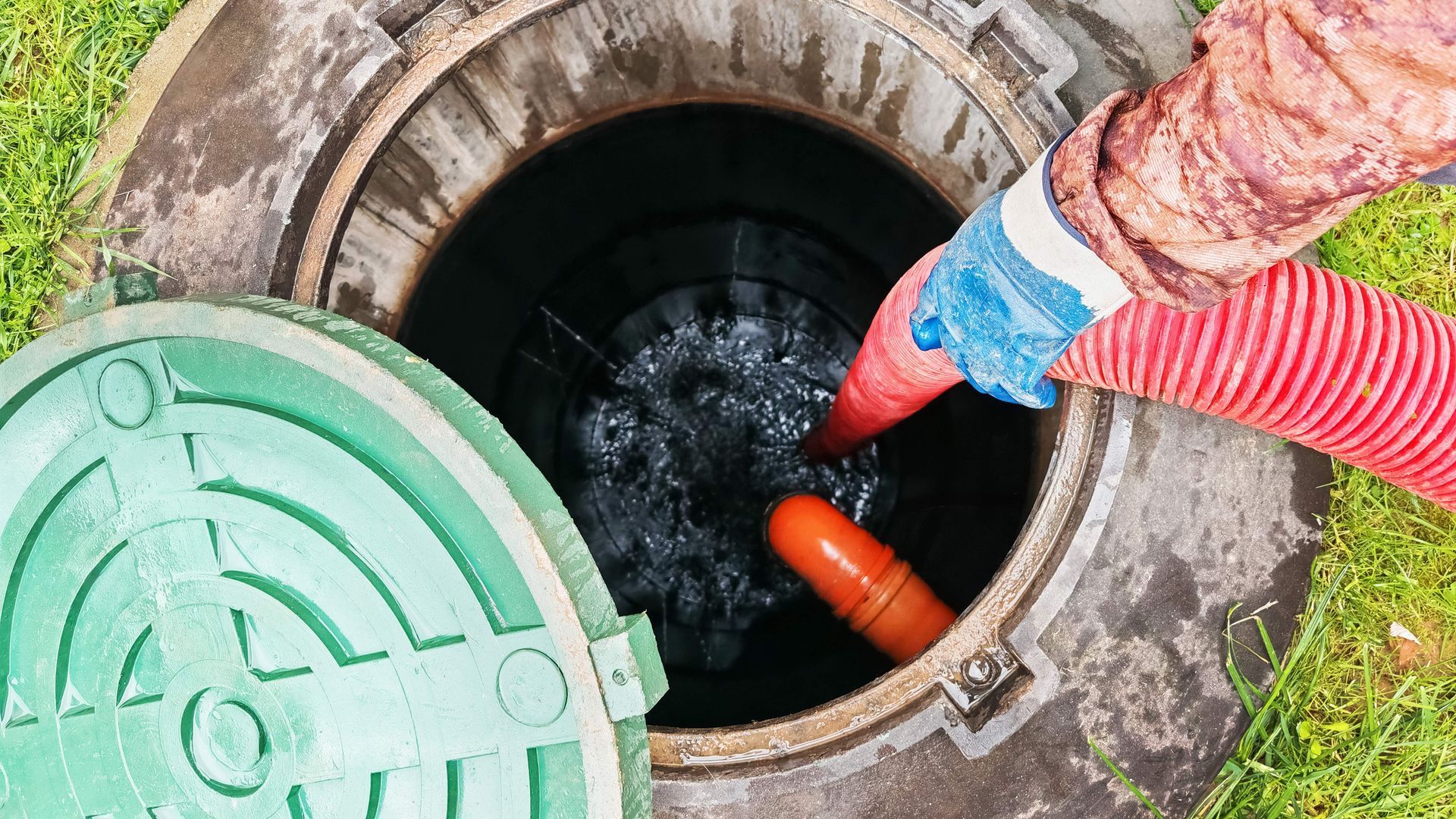A worker uses a hose and equipment to service a septic tank on a grassy area.