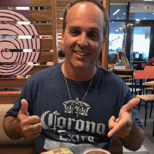 A man wearing a corona extra shirt is giving a thumbs up