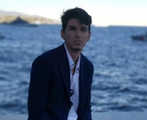 A man in a suit is sitting on a dock near the ocean.