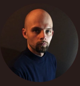 A bald man with a beard is wearing a blue sweater