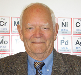A man in a suit and tie stands in front of periodic table signs