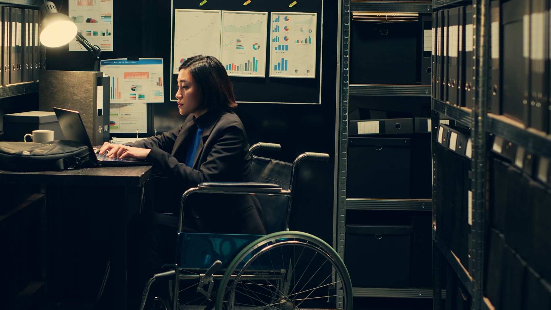 A woman in  wheelchair sat  at a desk using a laptop