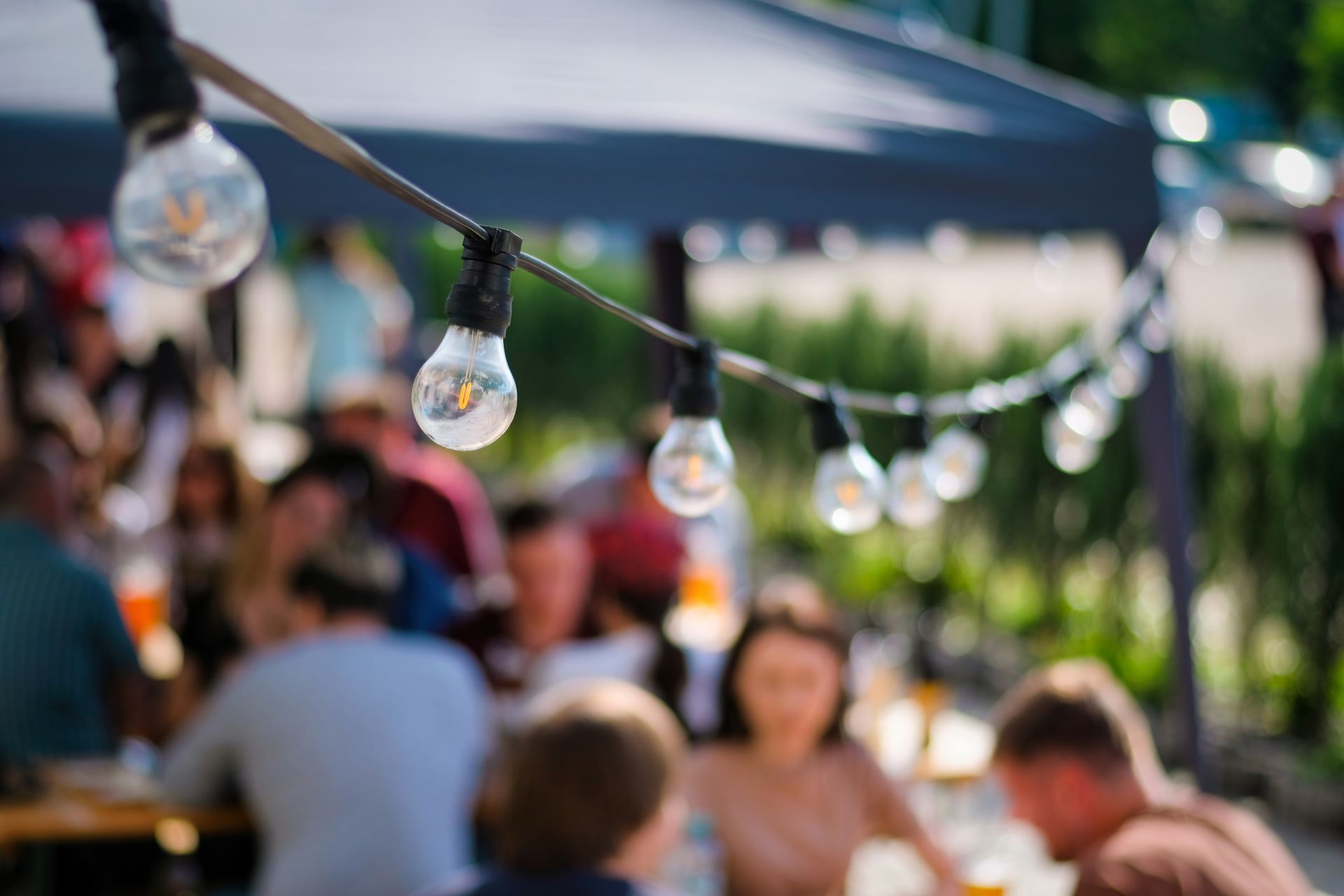 A group of people are sitting at tables under an umbrella at a public event.