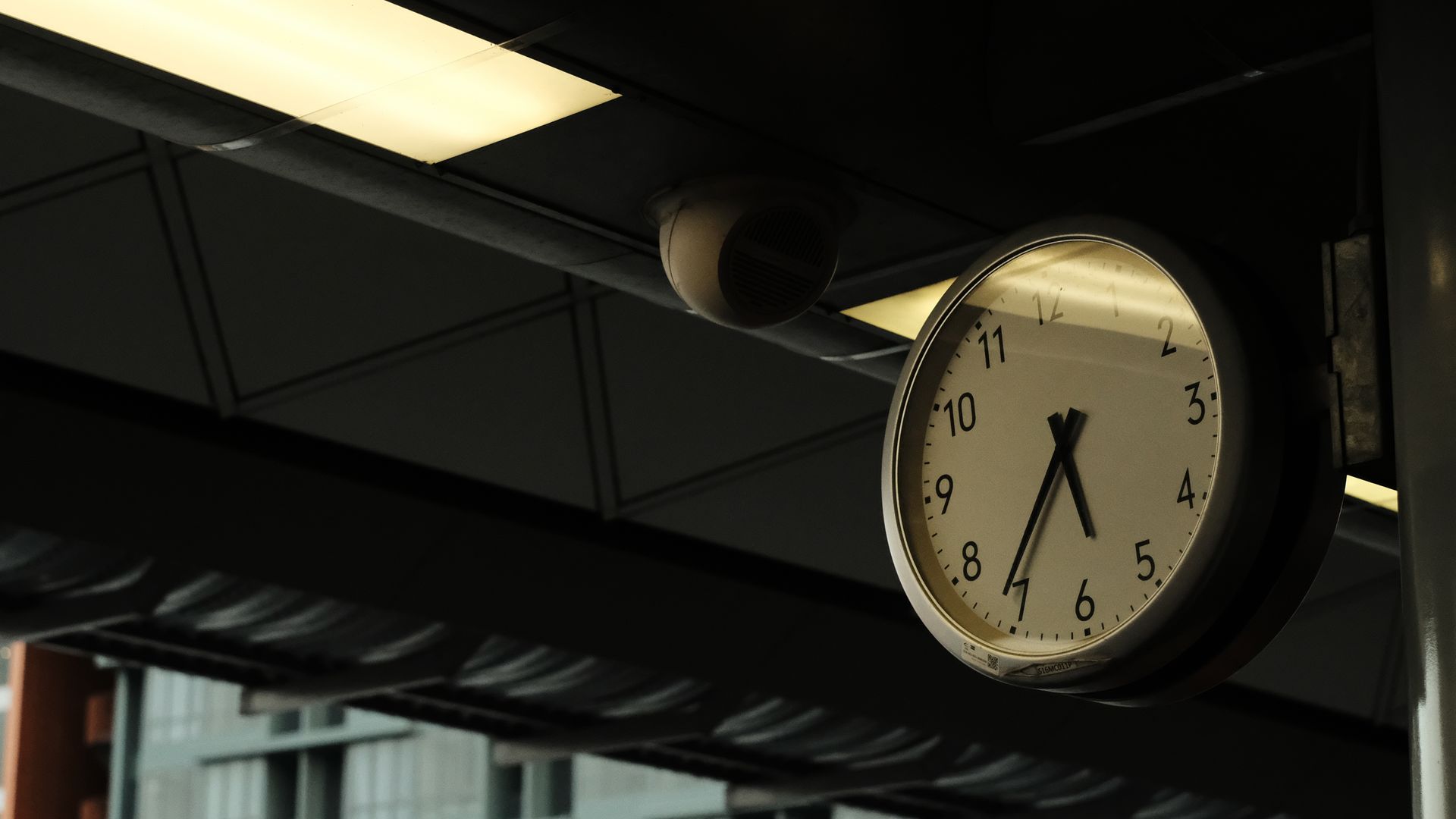 Clock on wall, security camera above. Clock on wall under awning, security camera above.