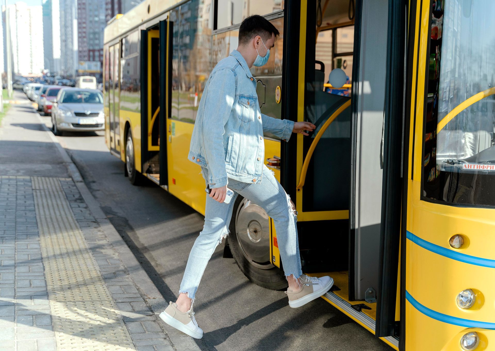 A man wearing a mask is getting on a yellow bus.