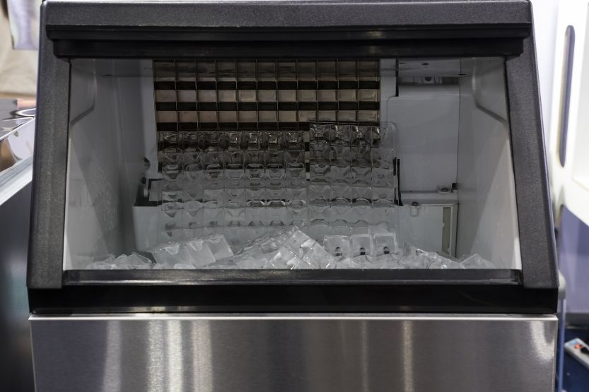 Commercial ice machine with ice cubes in a bin, stainless steel frame.