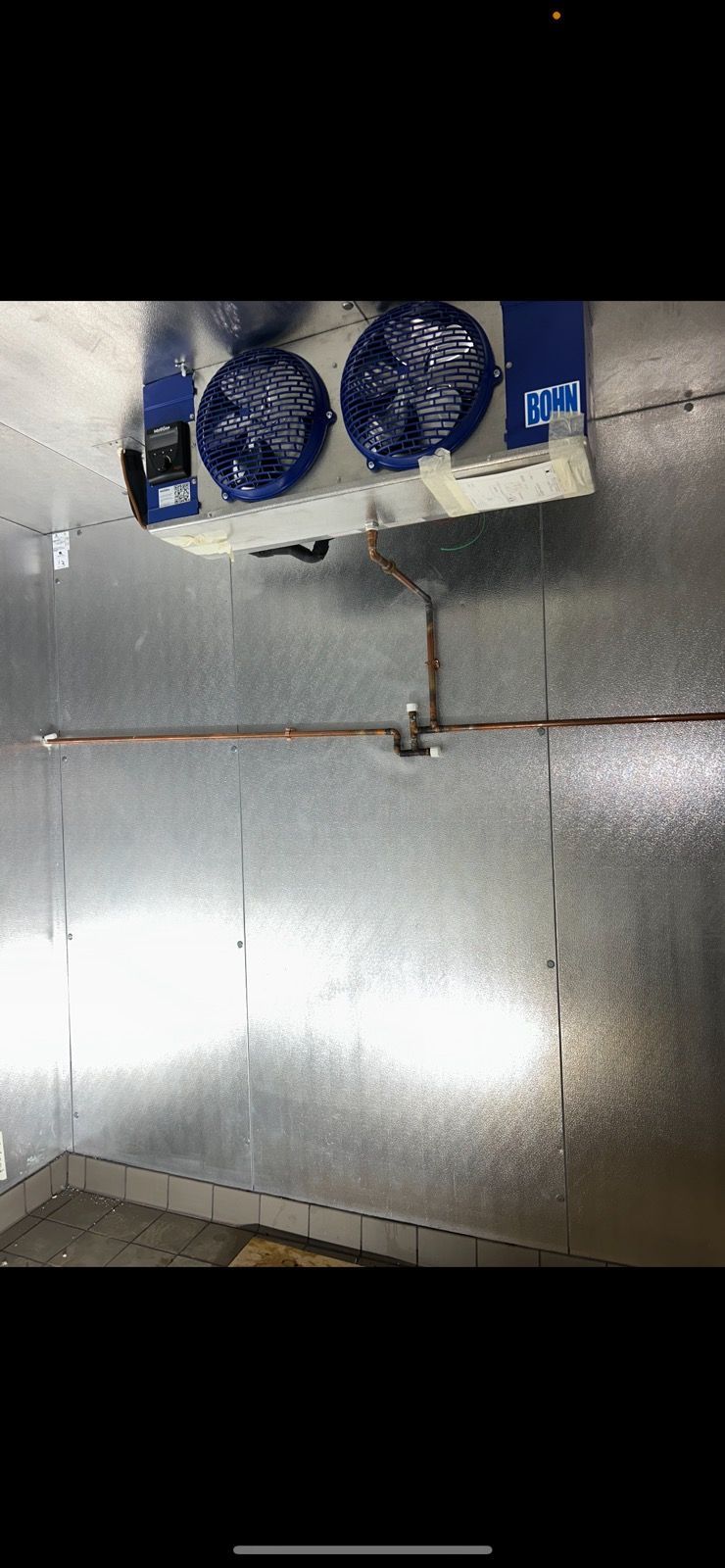 A refrigeration unit with two fans mounted on a silver wall. Copper piping is visible.