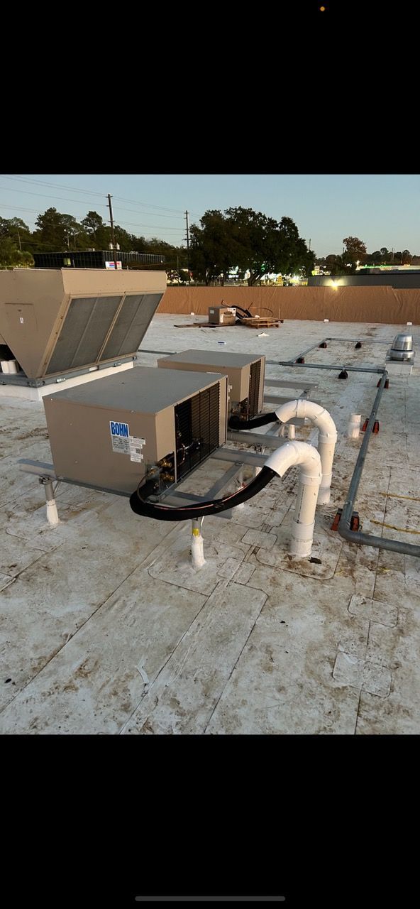 HVAC units on a commercial building rooftop. White pipes, black hoses, and the sky are visible.