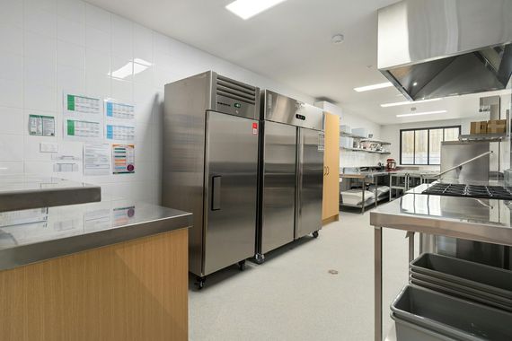 A long, dark grocery aisle with glass-doored refrigerators lining both sides, lit with blue and red hues.