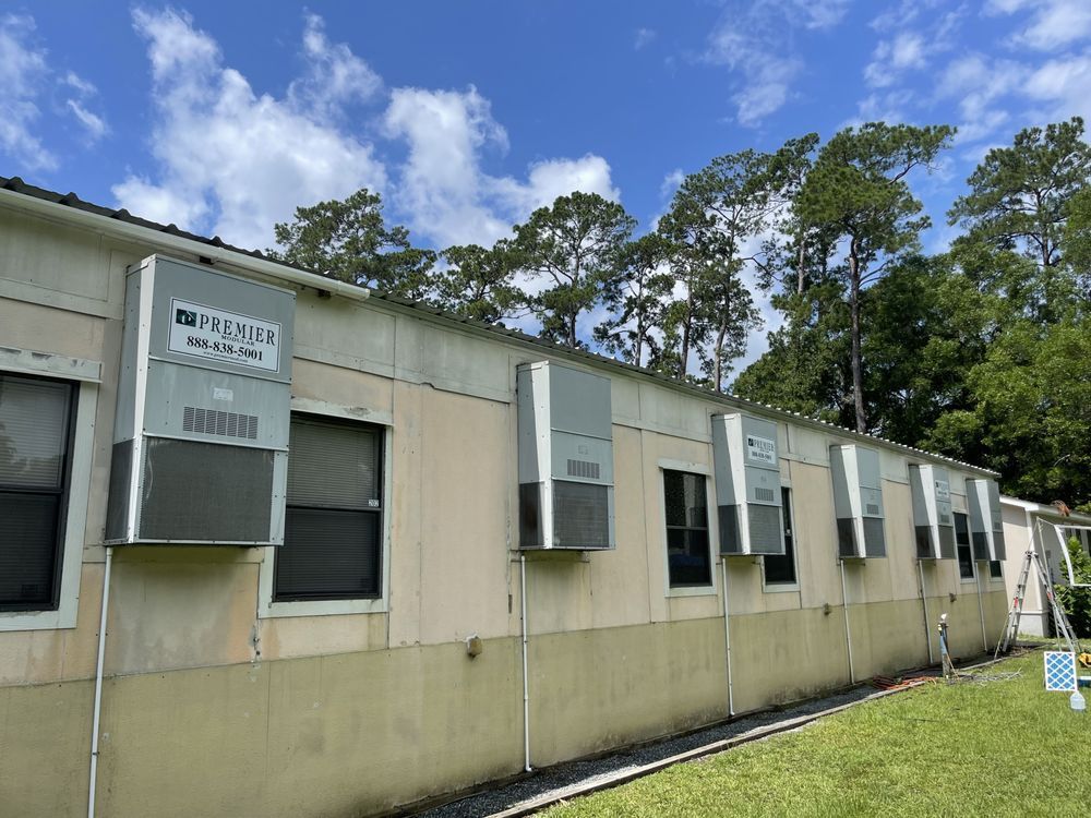 Exterior of a building with multiple window air conditioners, under a partly cloudy sky.
