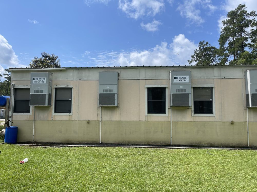 A tan, single-story building with multiple AC units and windows under a blue sky.