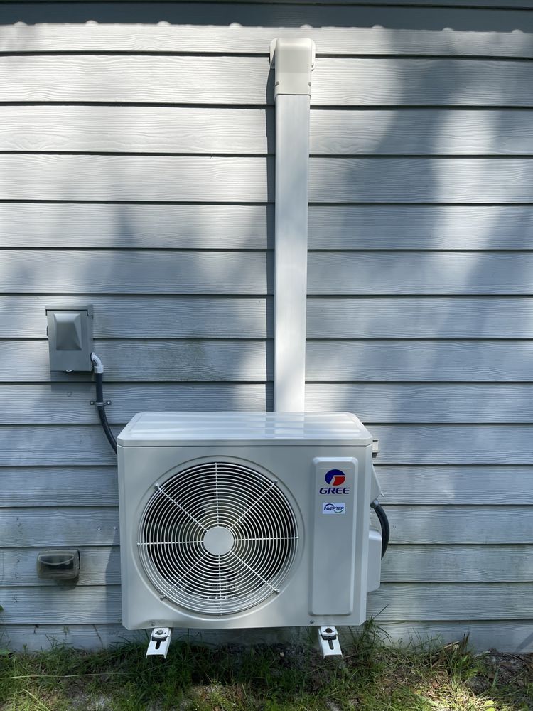 White air conditioning unit mounted on a gray wall with a vent pipe above it.