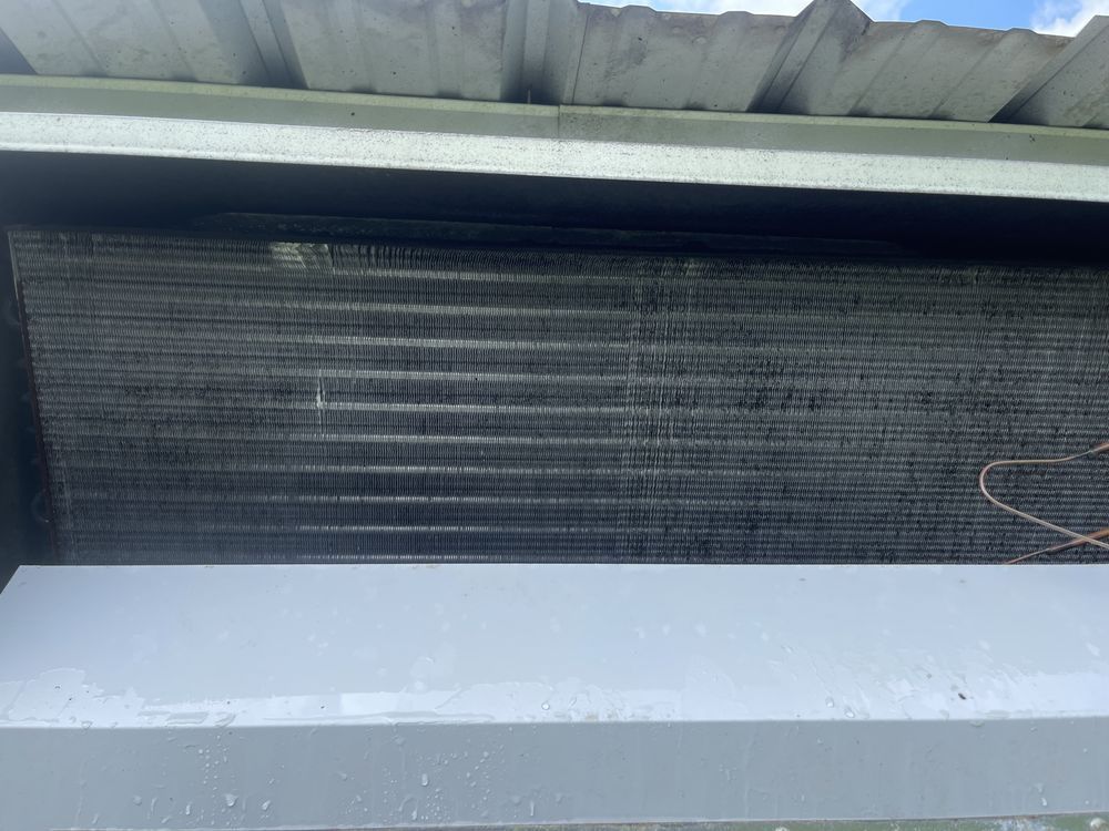 Air conditioning unit's evaporator coil, gray and dirty, under a metal overhang.