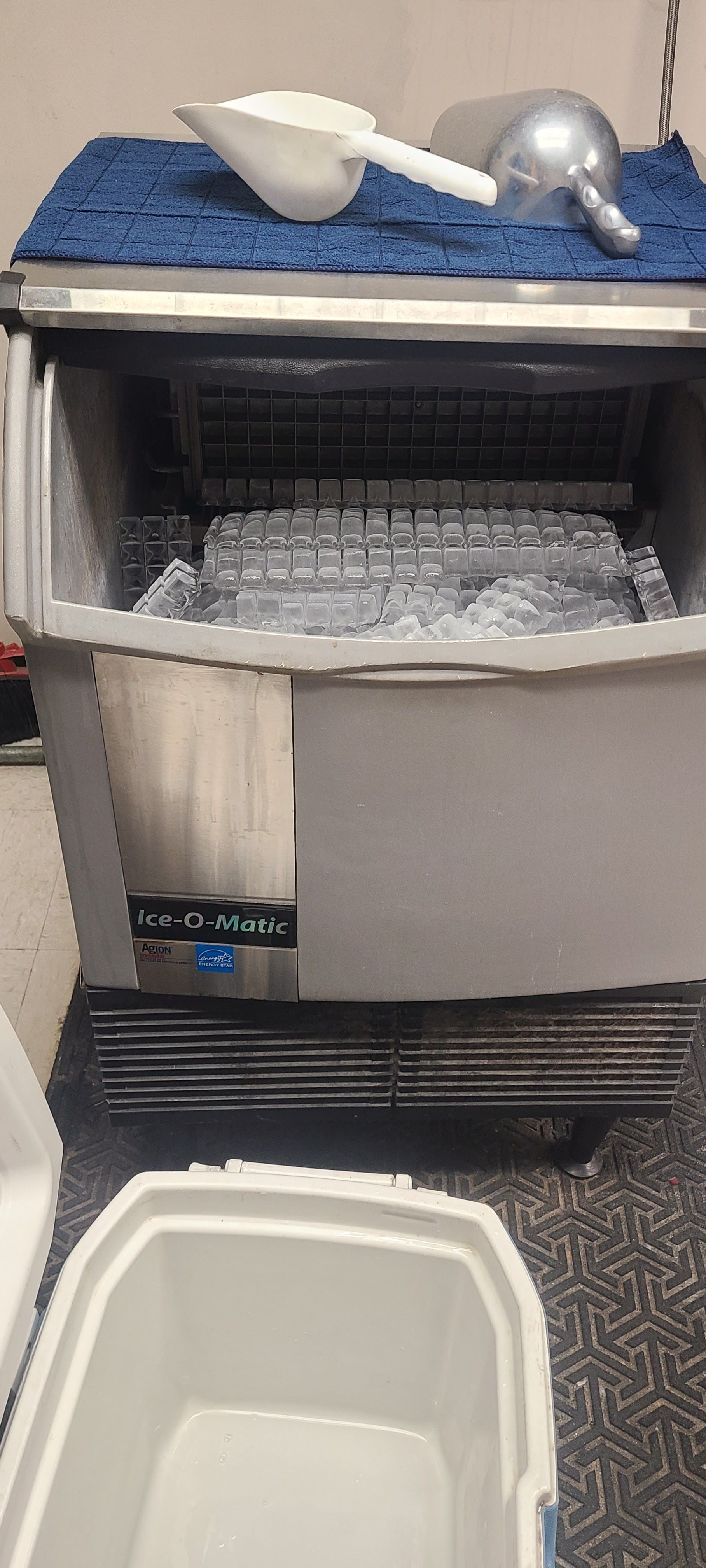 An ice machine with a scoop and bin, partially filled with ice.