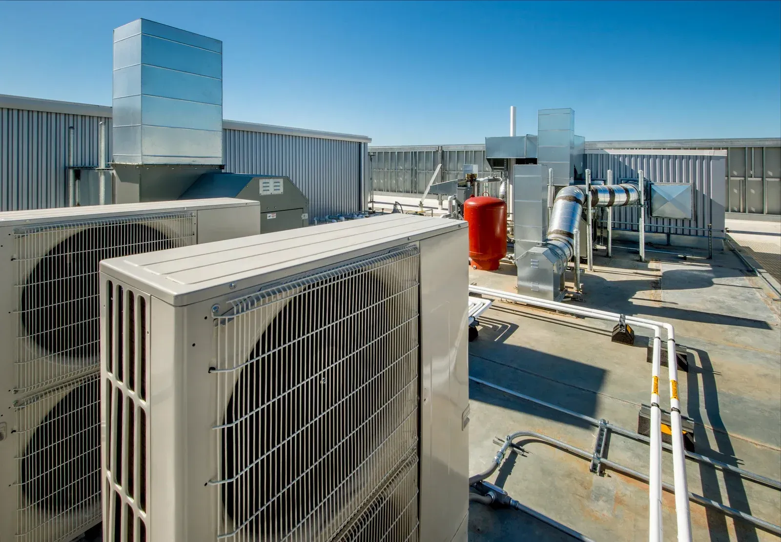 HVAC units on a rooftop with metal ductwork and a clear blue sky.