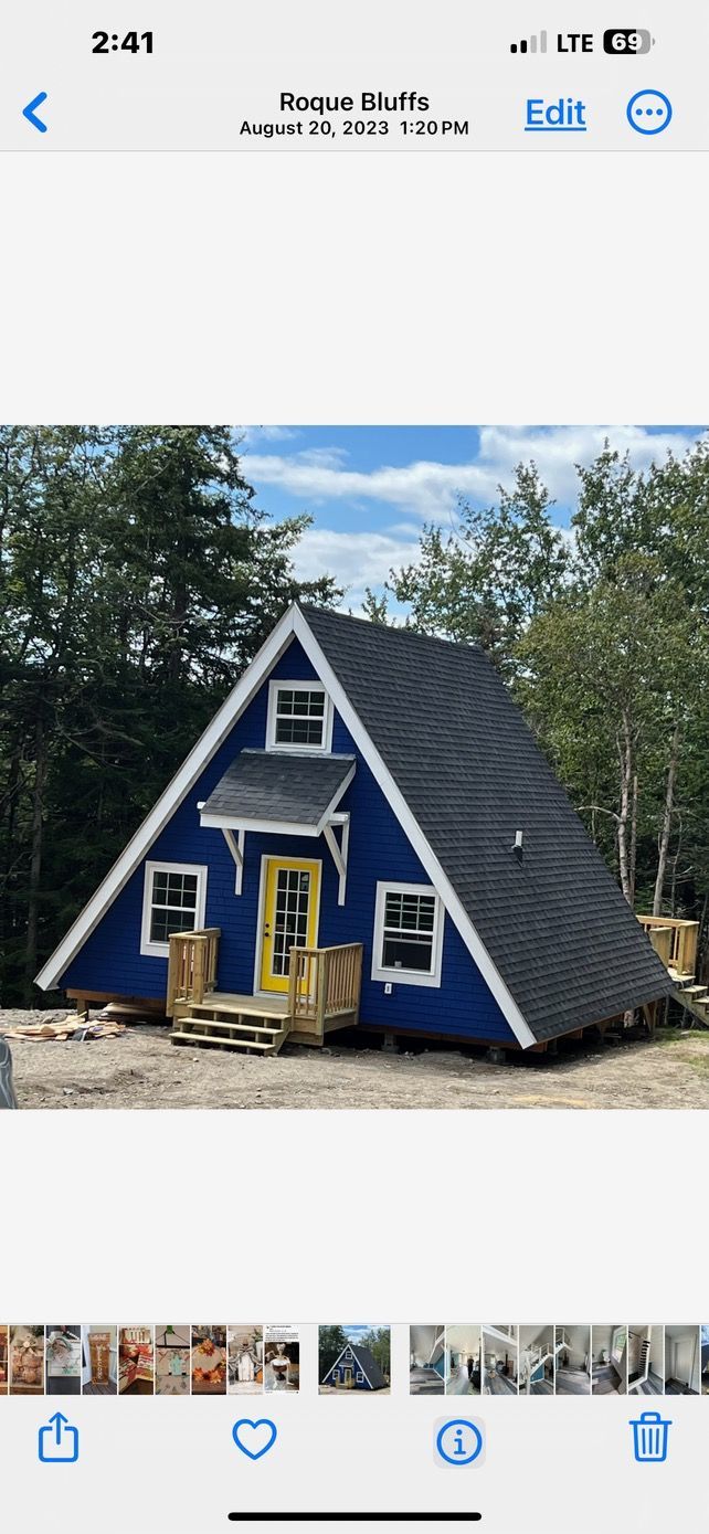 A blue a frame house with a yellow door is sitting in the middle of a forest.