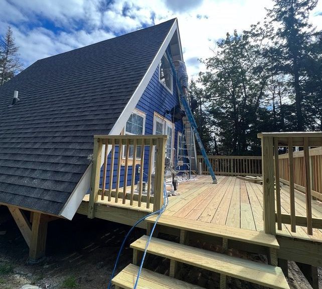 A blue house with a wooden deck is being painted.