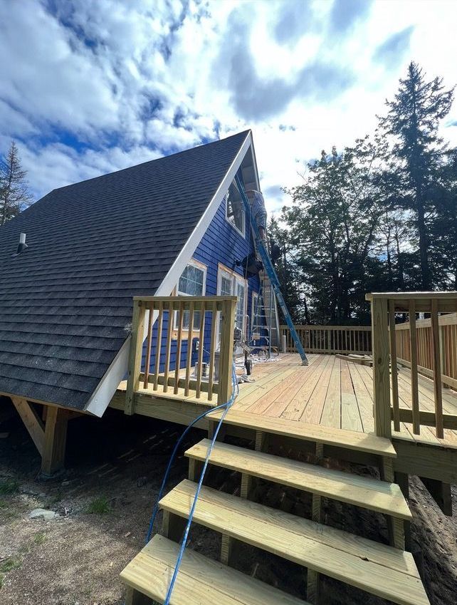 A blue house with a wooden deck and stairs leading to it.