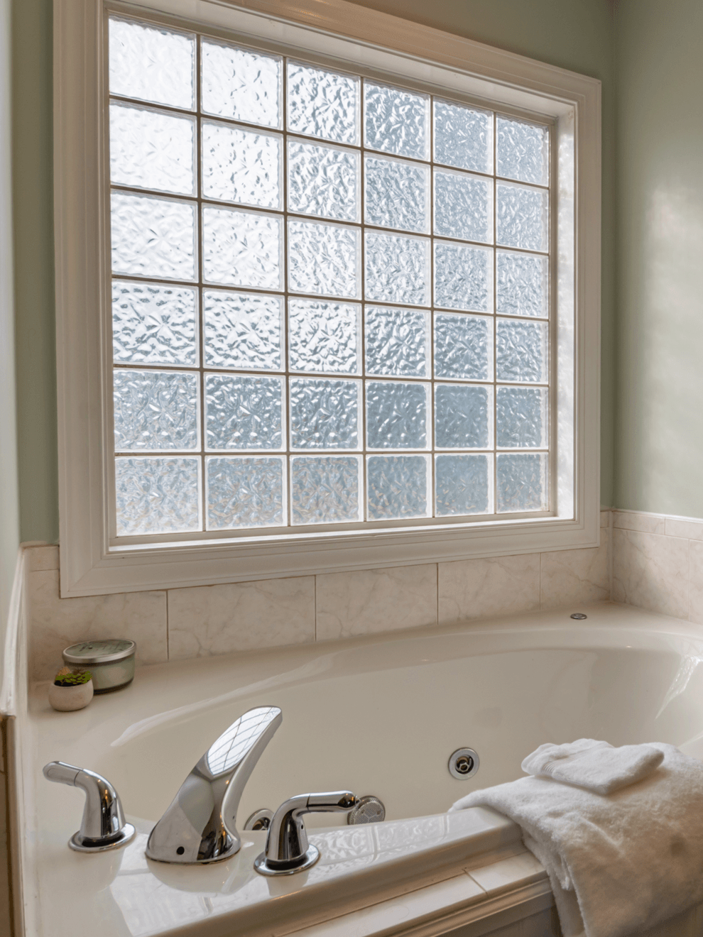 A bathtub in a bathroom next to a window with privacy glass.