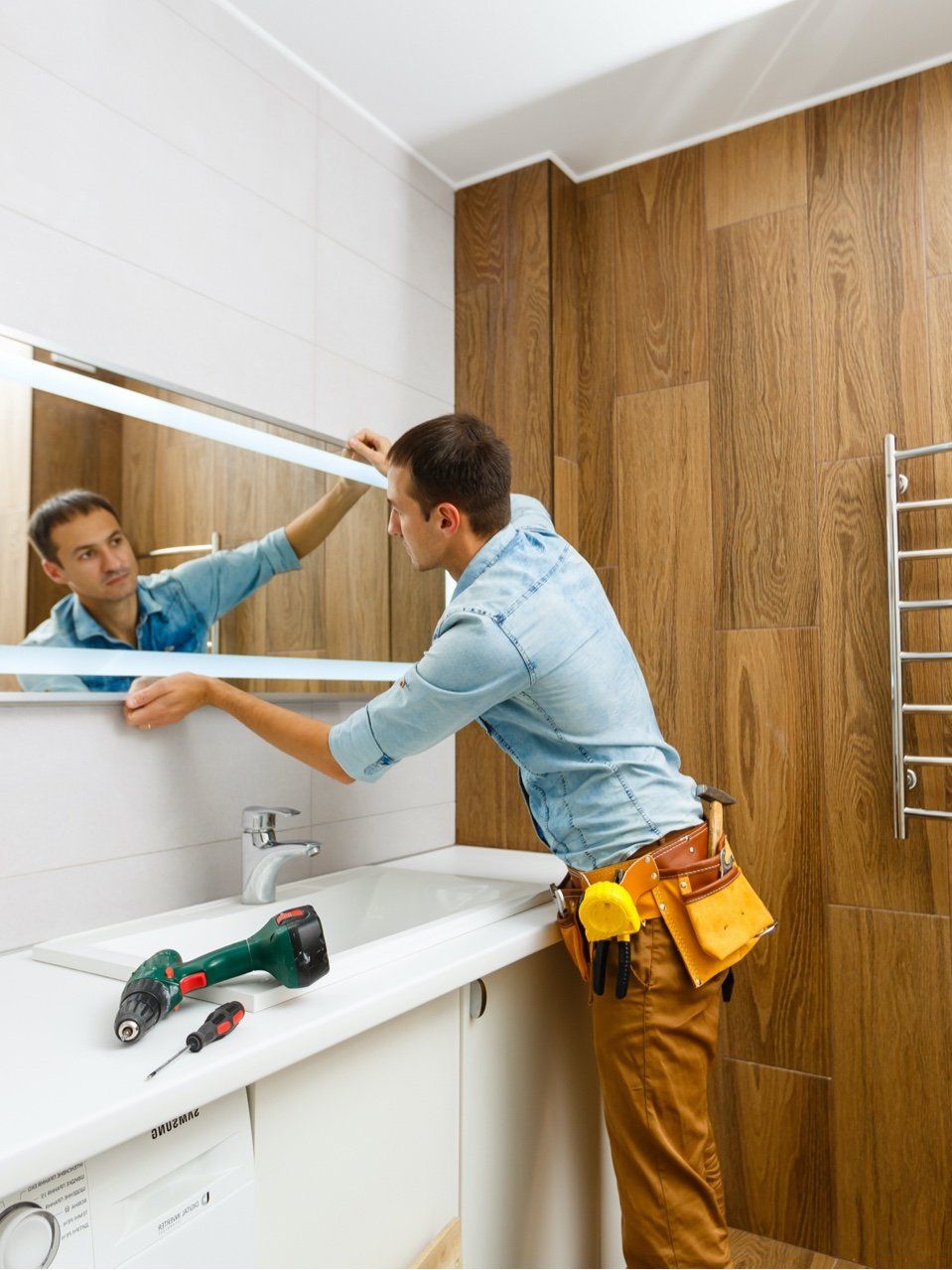 a contractor installing a bathroom mirror above a vanity