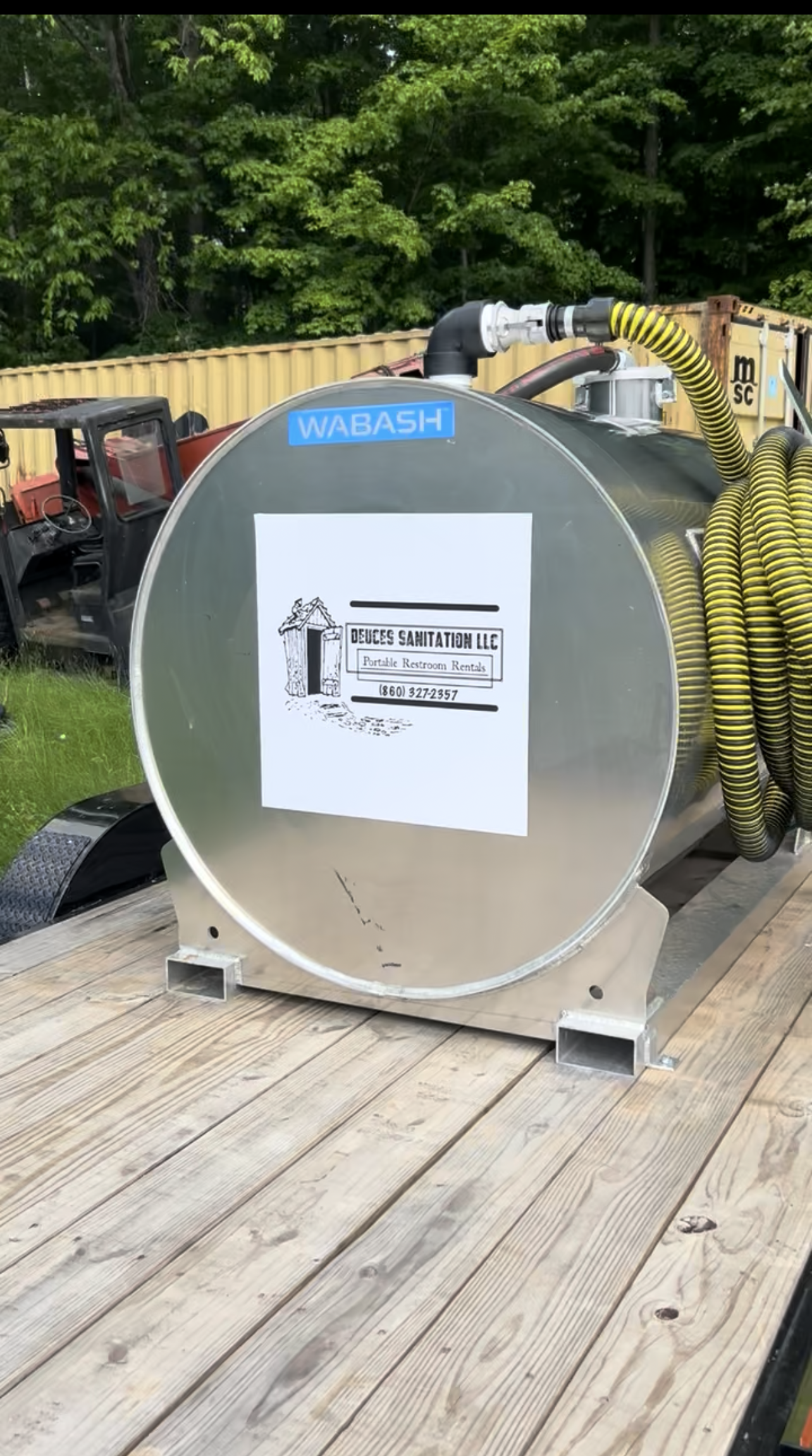A large silver tank on a wooden trailer bed; a yellow hose is coiled beside it.