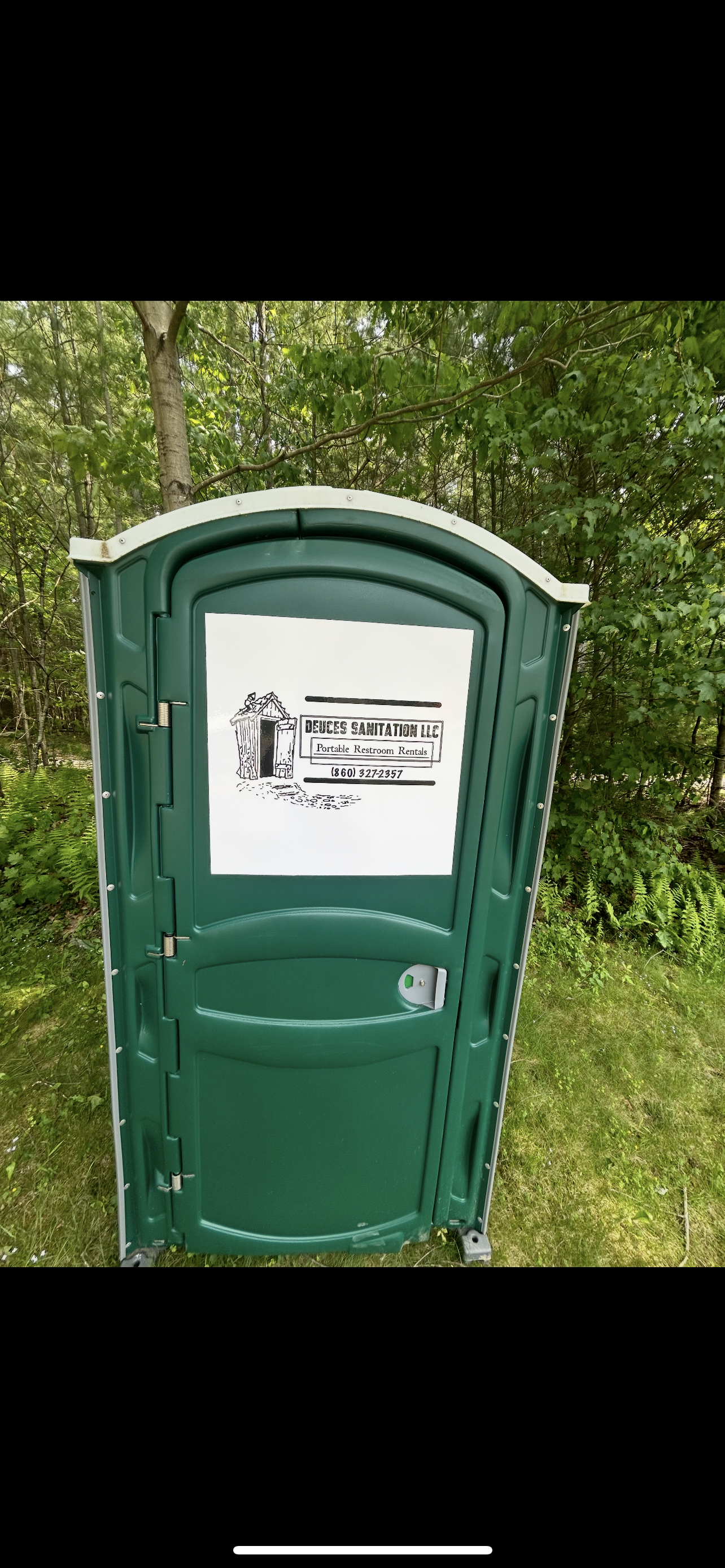 Green portable toilet with a white sign, set in front of greenery.