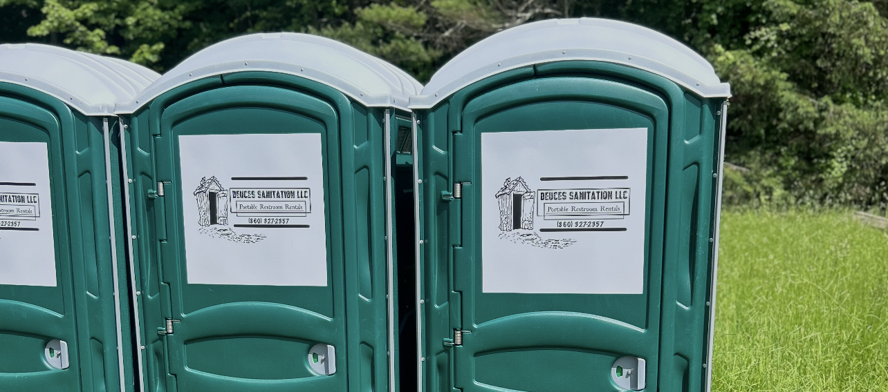 Three green portable toilets lined up in a grassy field.