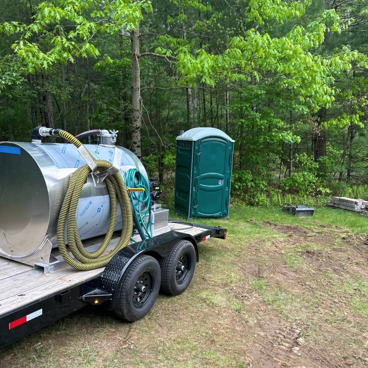A trailer with a stainless steel tank and a green portable toilet on it.