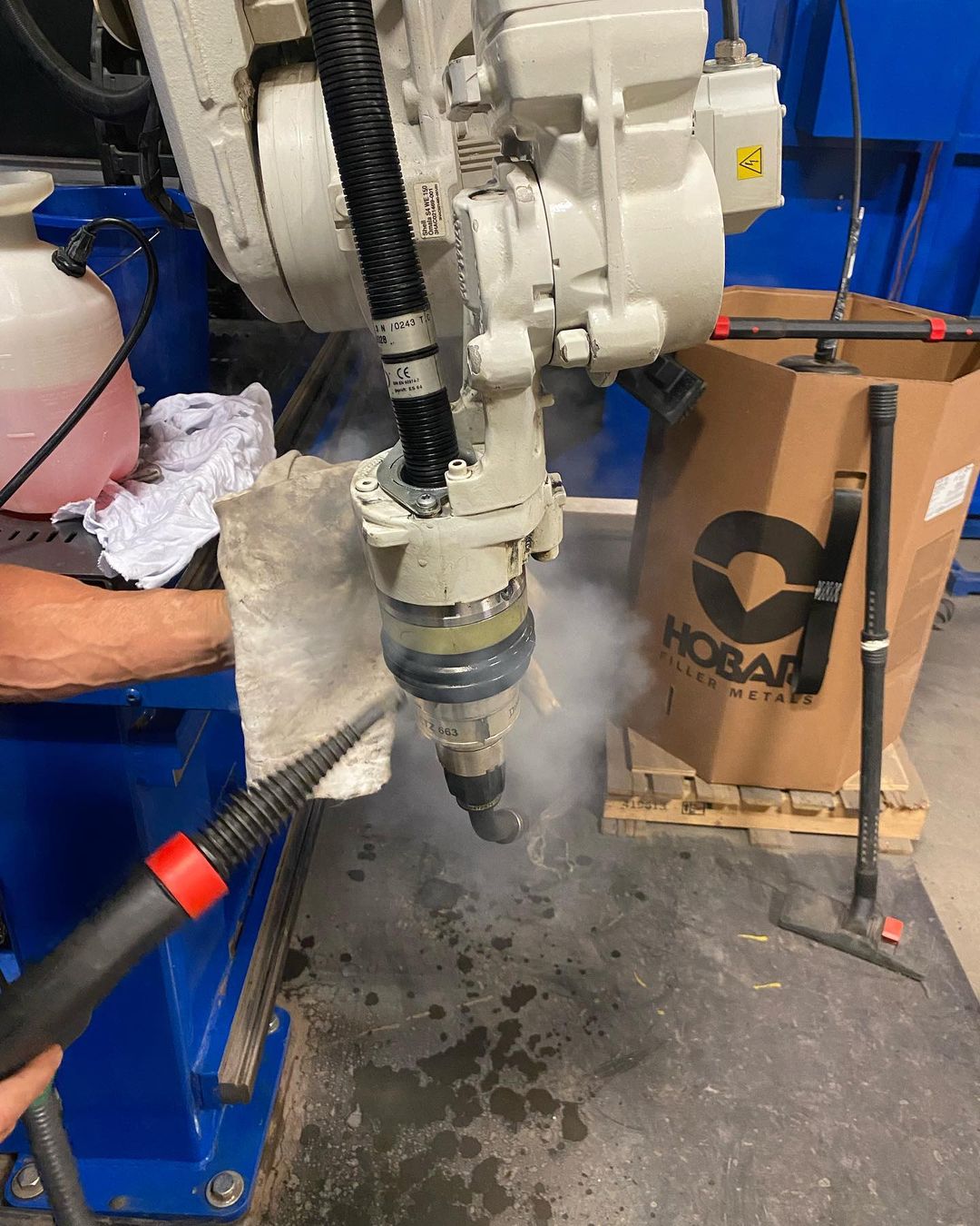 Une personne nettoie un bras robotique avec un nettoyeur à vapeur.