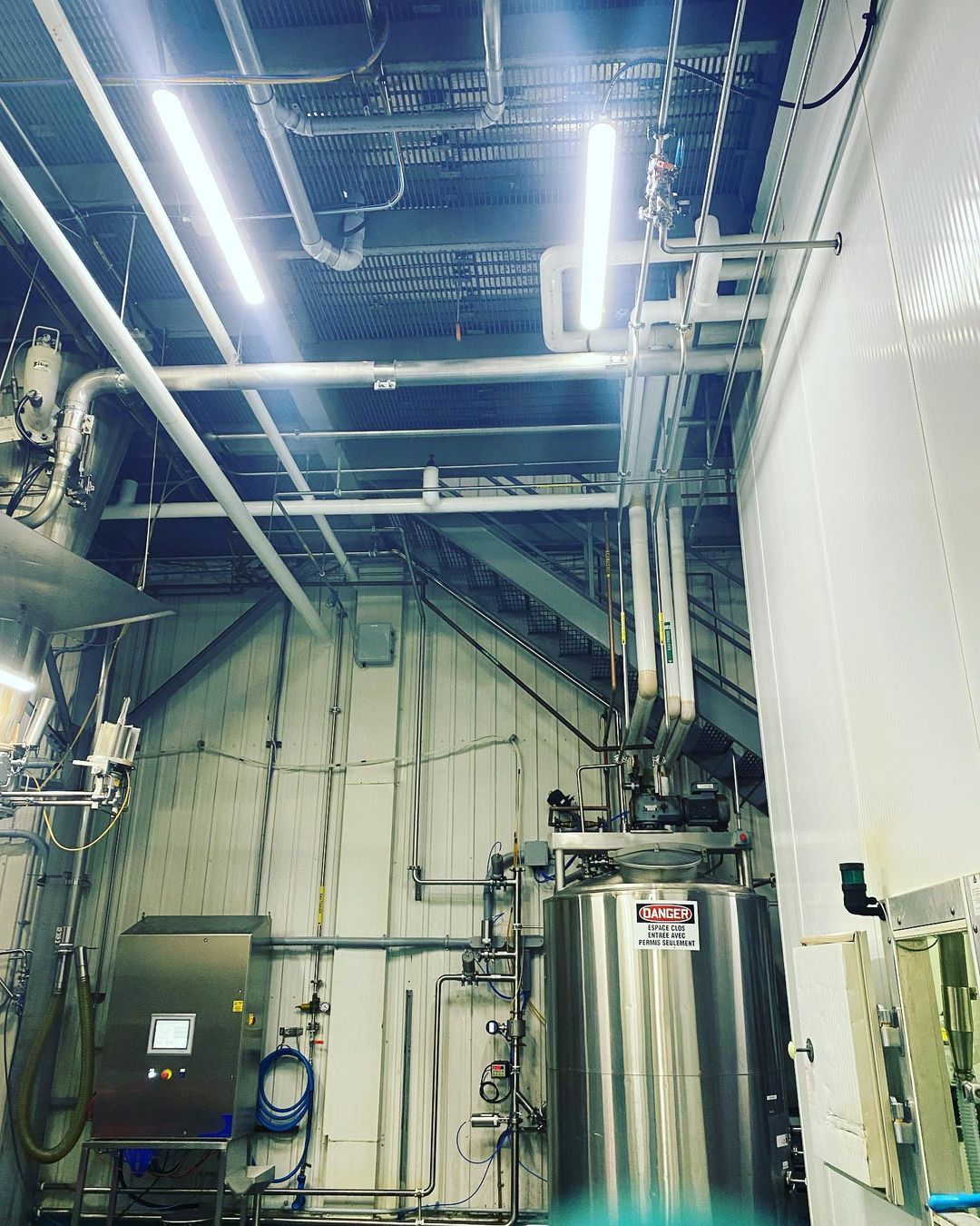 Un grand réservoir en acier inoxydable se trouve dans une pièce avec beaucoup de tuyaux.