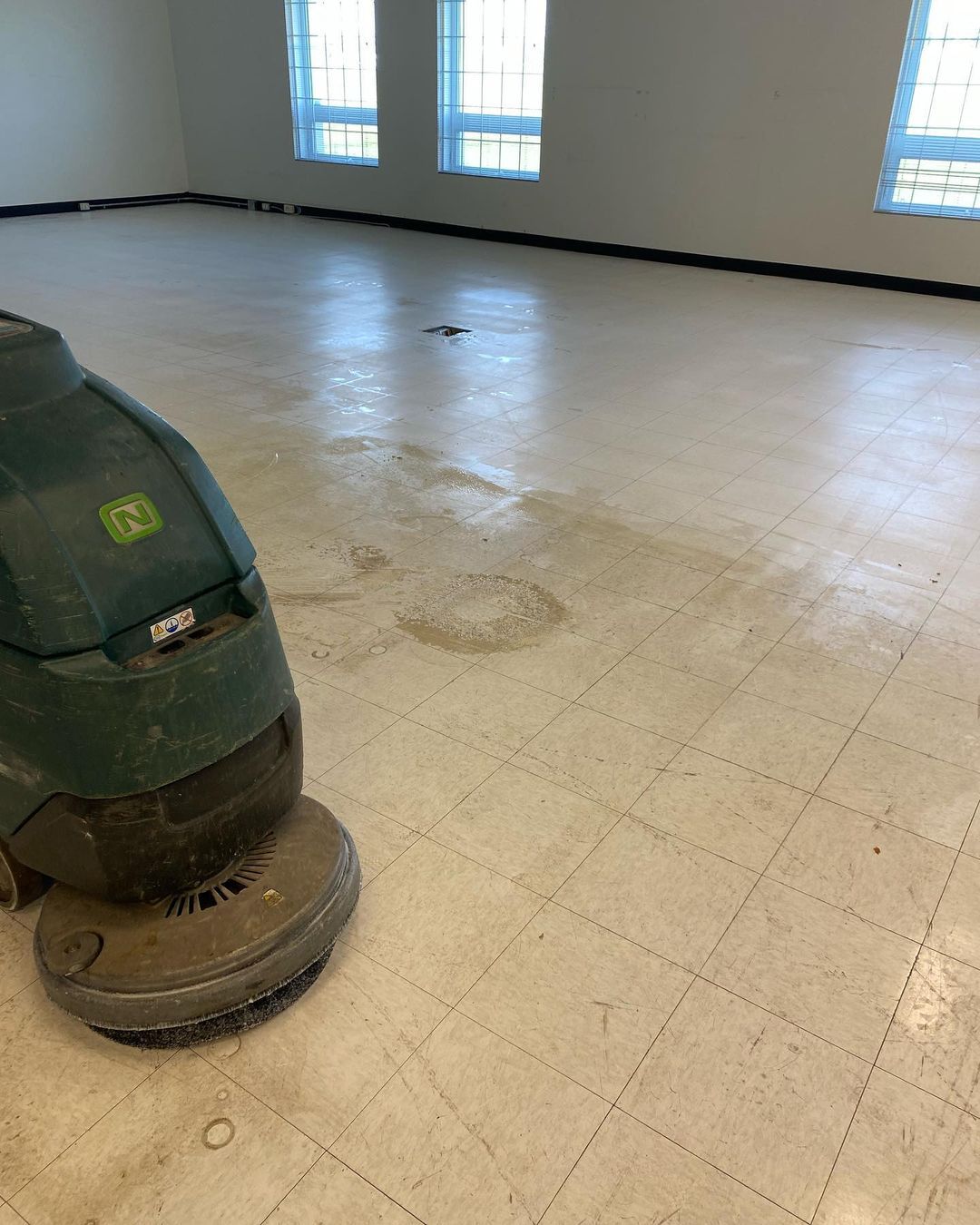 Une machine nettoie un sol carrelé dans une pièce vide.
