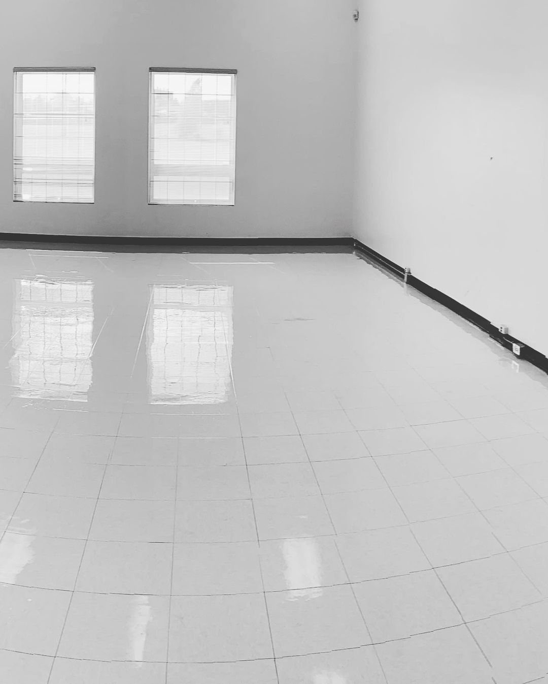 Une photo en noir et blanc d'une pièce vide avec des sols et des fenêtres carrelés.