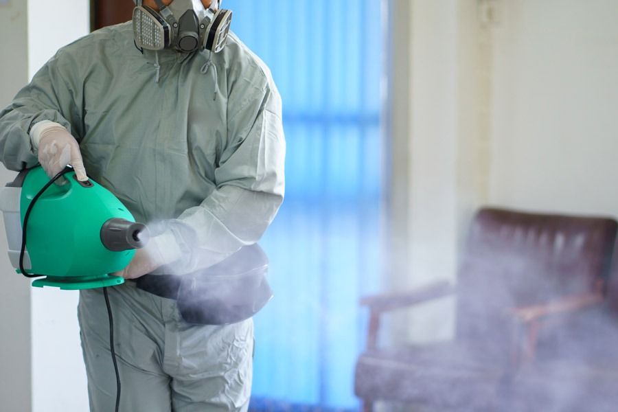 Un homme en tenue de protection désinfecte une pièce avec un pulvérisateur.