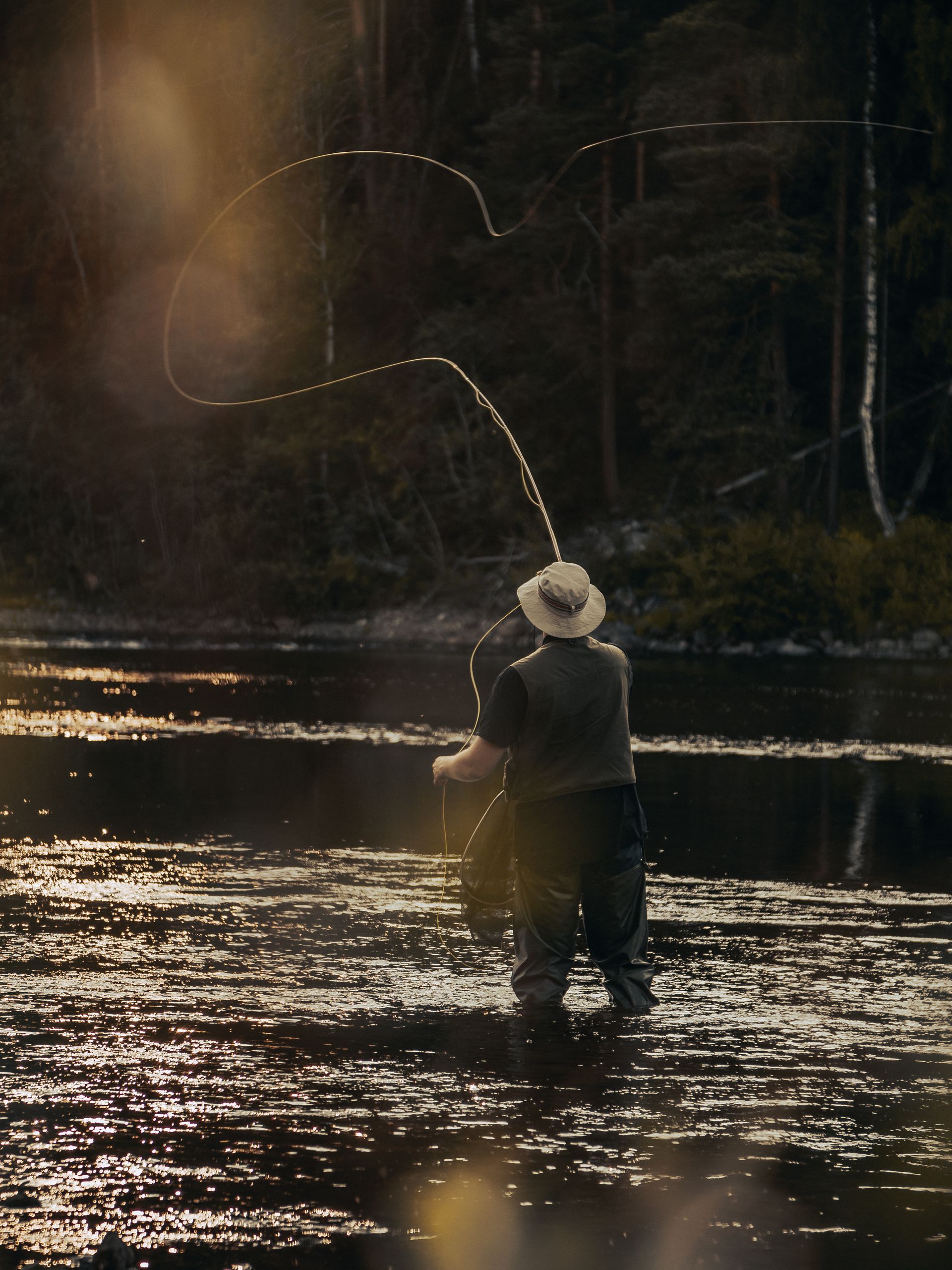 A man in a cowboy hat is fishing in a river