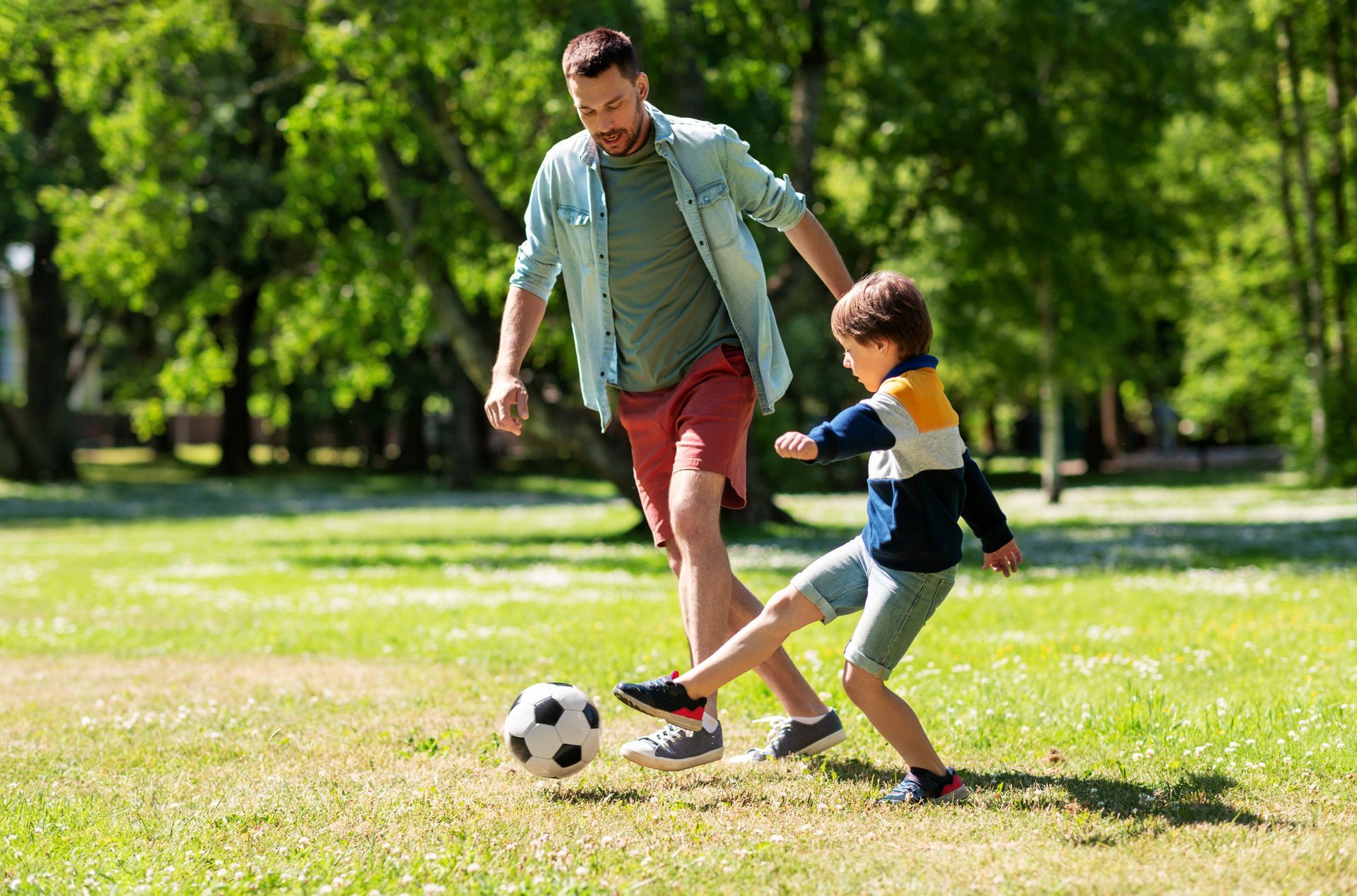 A man and a boy are playing soccer in a park.