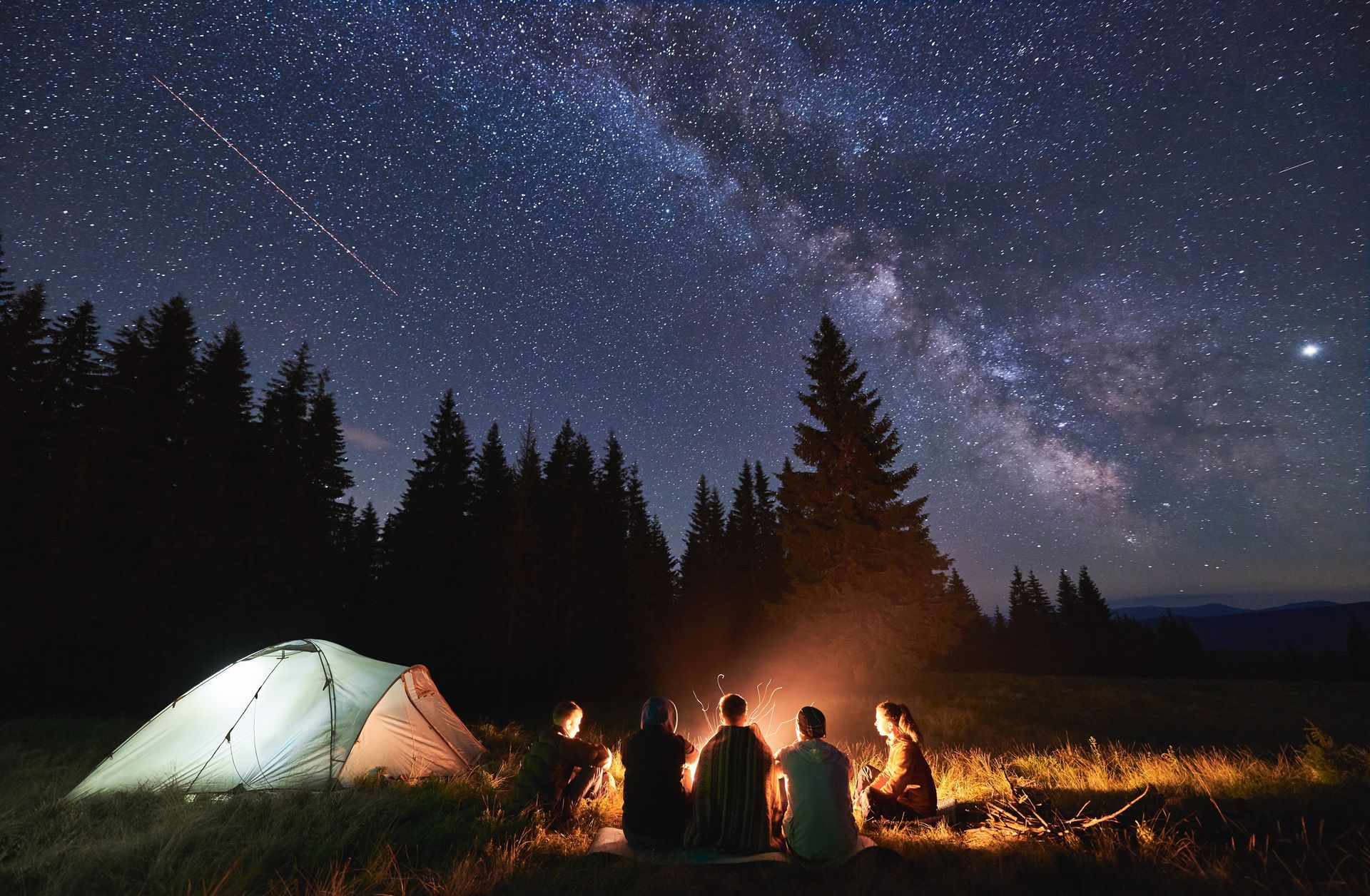 A group of people are sitting around a campfire under a starry night sky.