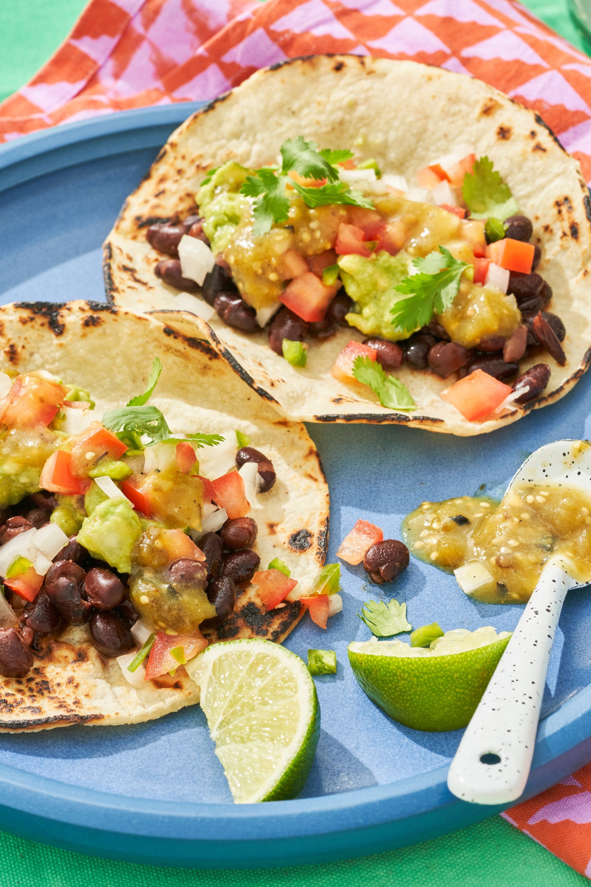 Three tacos on a blue plate with limes and salsa.