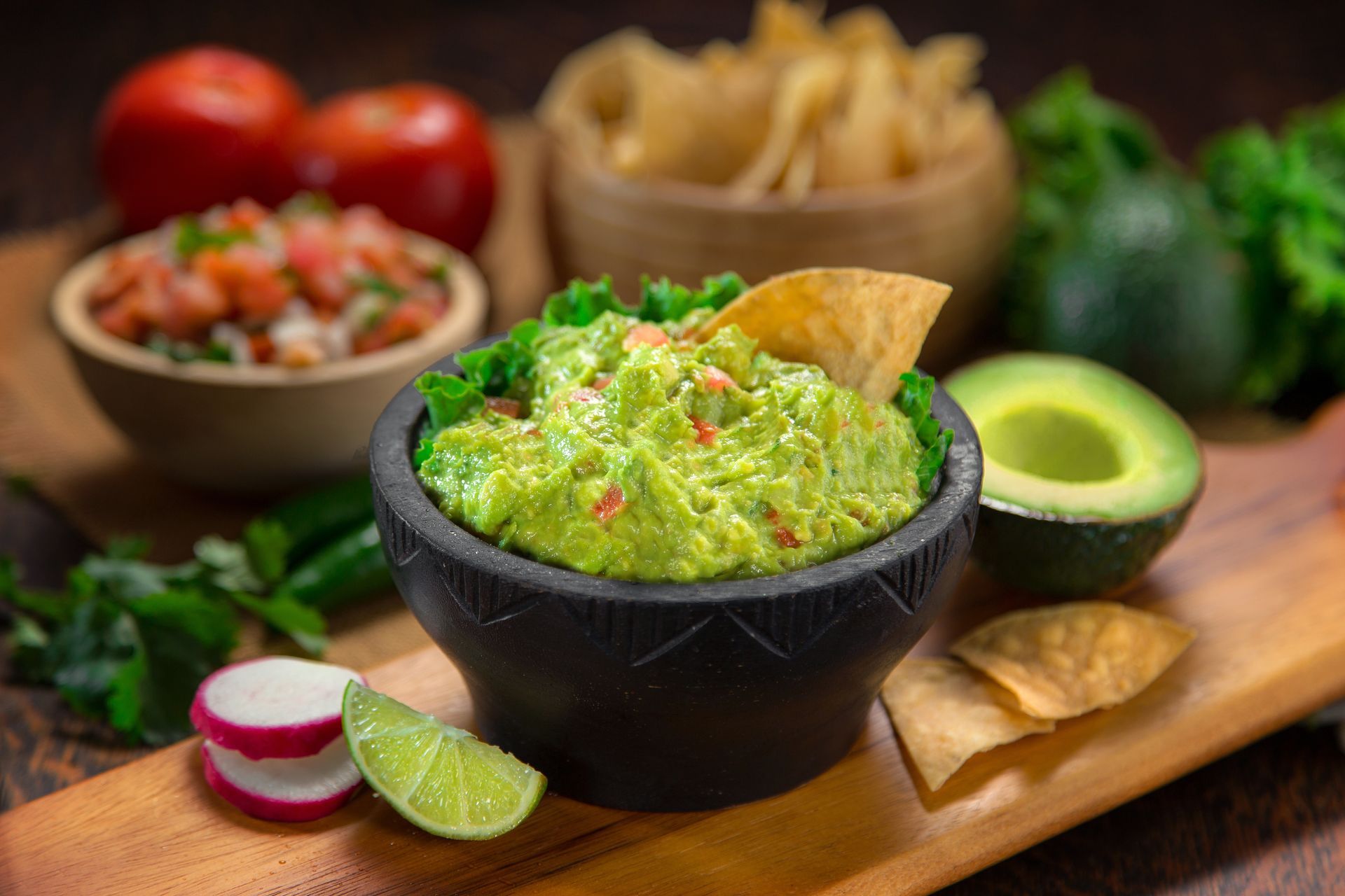 A bowl of guacamole with a tortilla chip in it on a wooden cutting board.