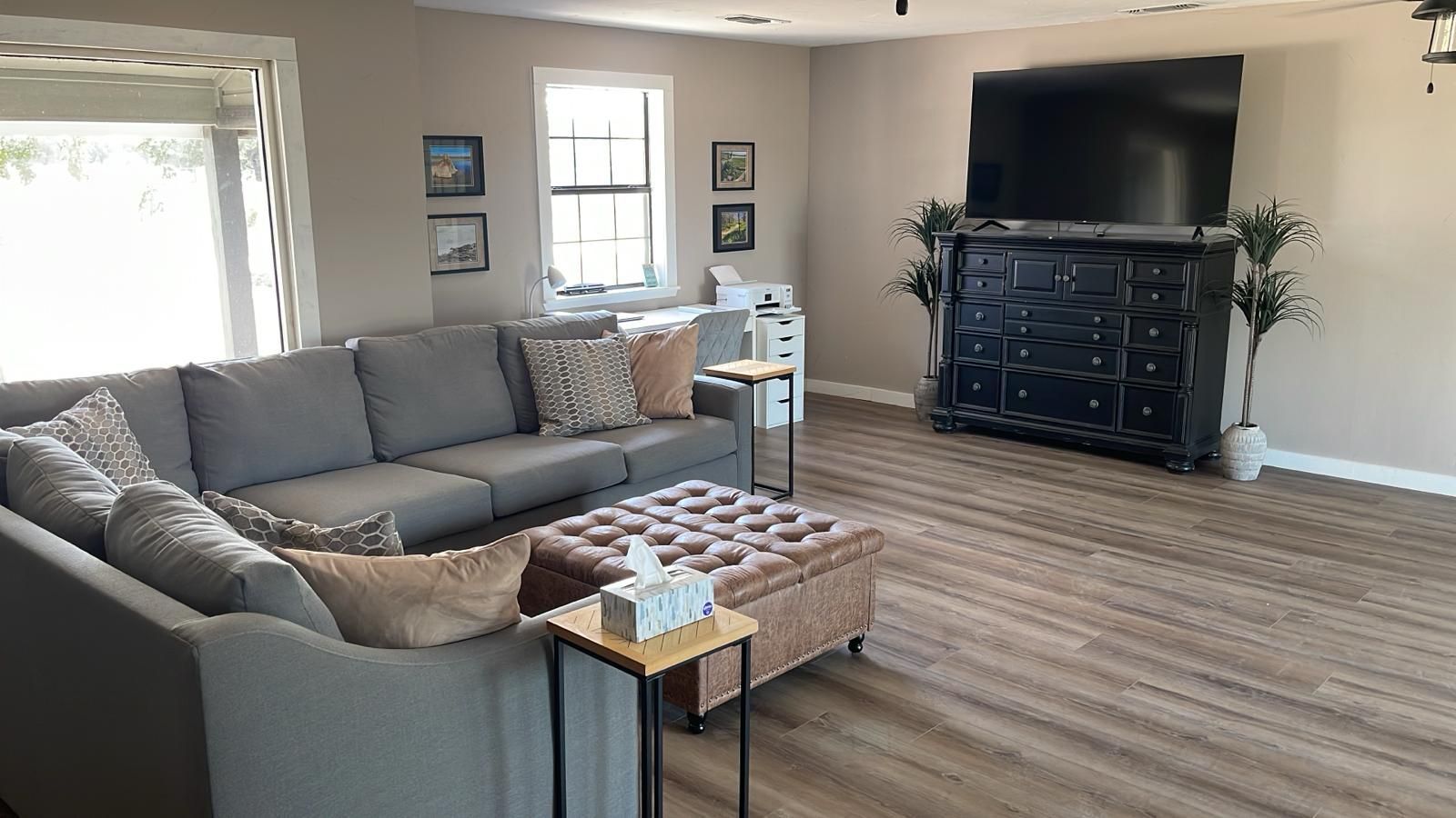 Gray sectional sofa in a living room with a large TV, black cabinet, and ottoman.