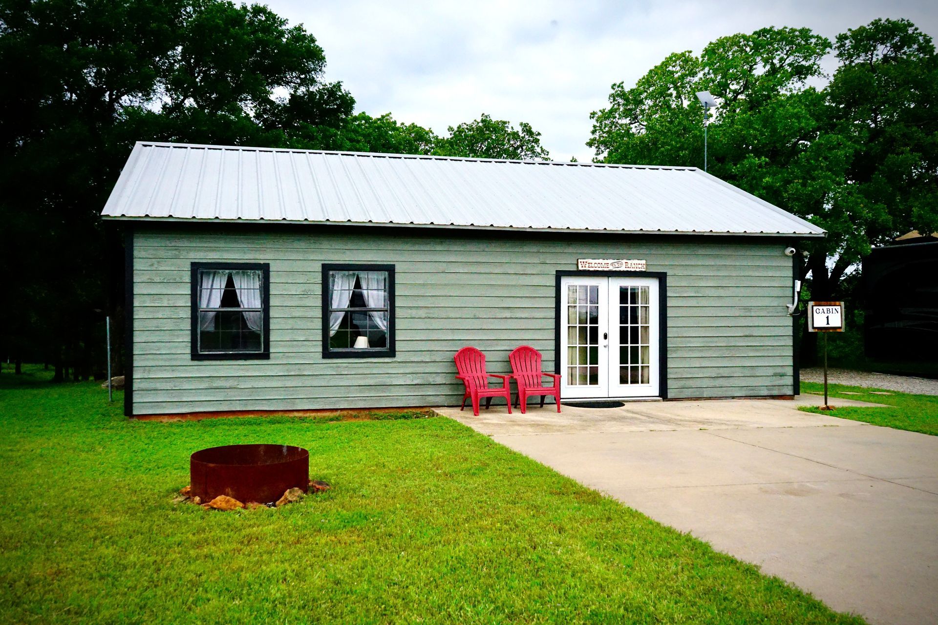 Green cabin with red chairs outside double doors, gray roof. Sign reads 