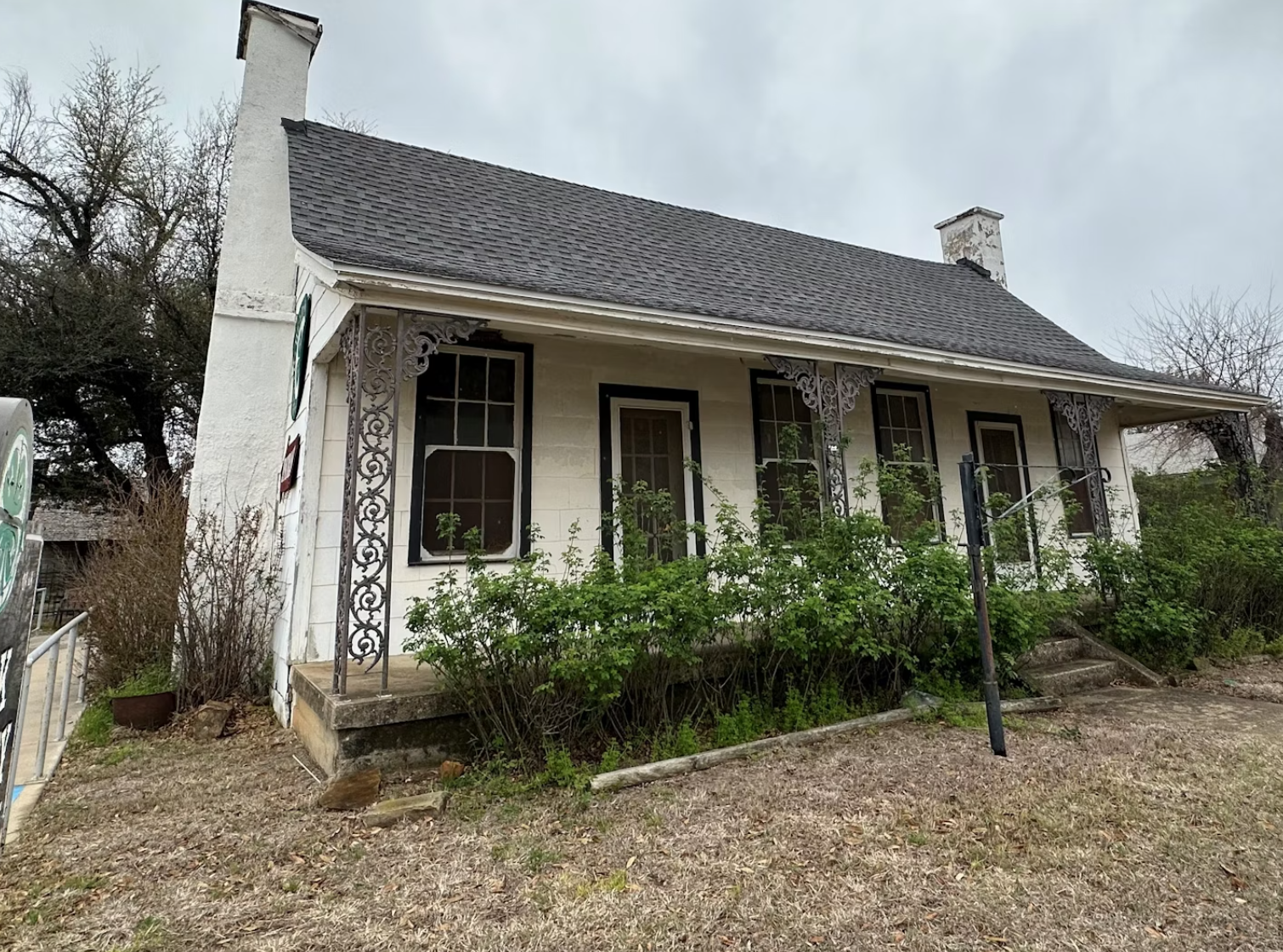 A small white house with a gray roof is sitting in the middle of a dirt field.