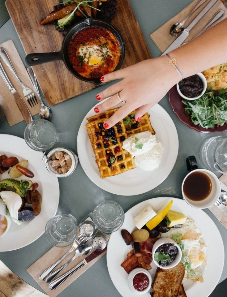 A person is reaching for a waffle on a table full of food.