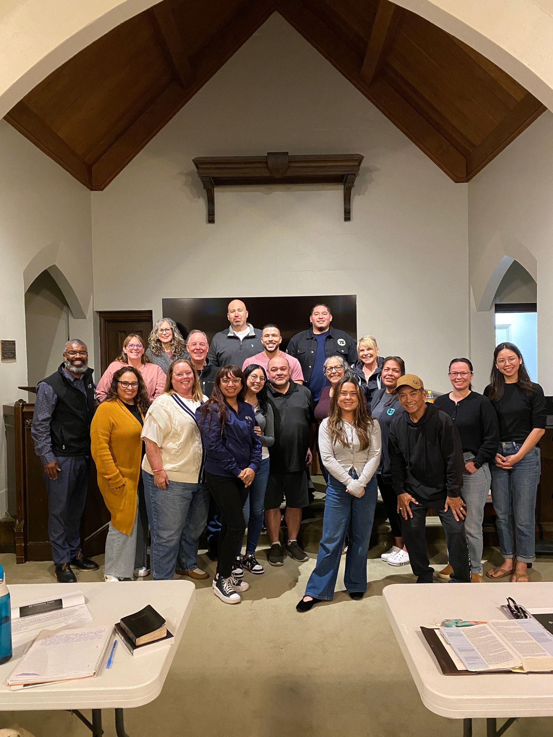 Group of people posing in a wood-paneled room with tables. They appear to be smiling at the camera.