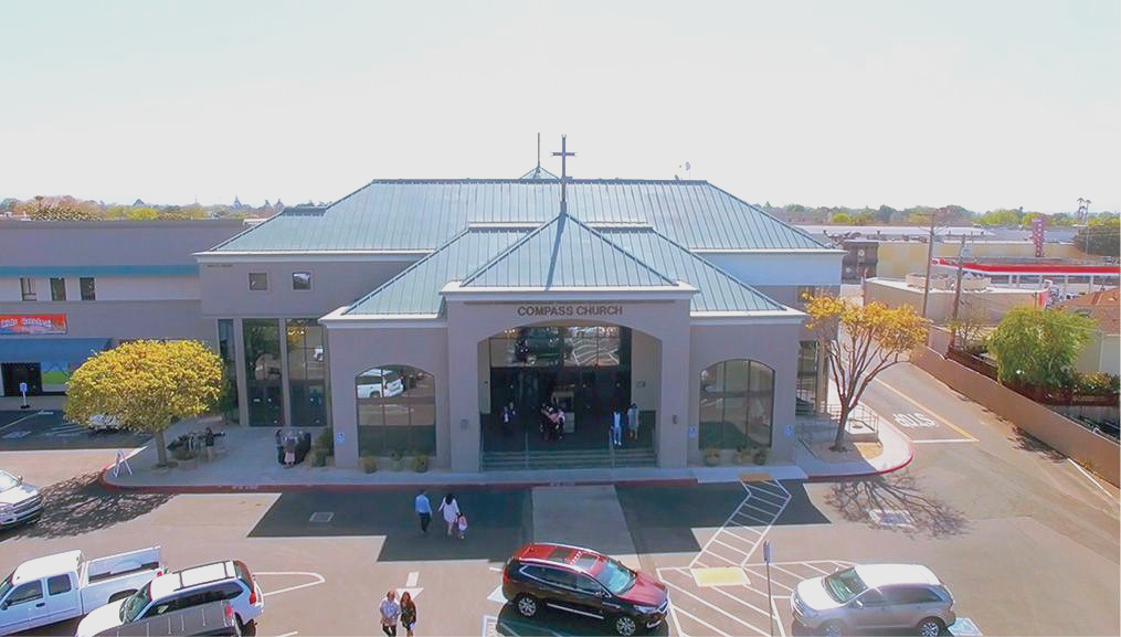 Compass Church building in Salinas & Monterey County with a teal roof and cross, people walking near the entrance.