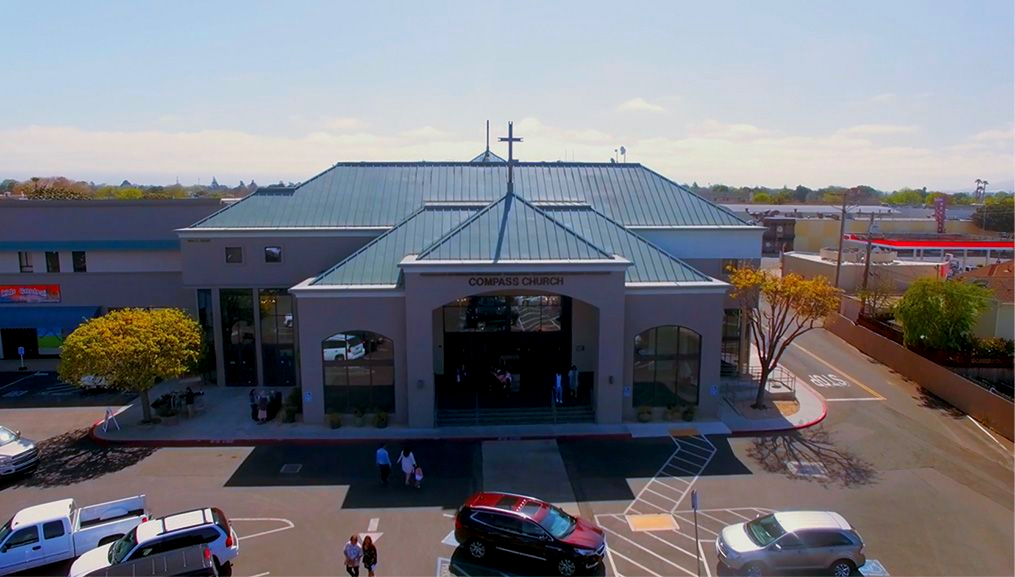 Compass Church building with a cross on top, people outside, and cars parked. in Salinas and Monterey County