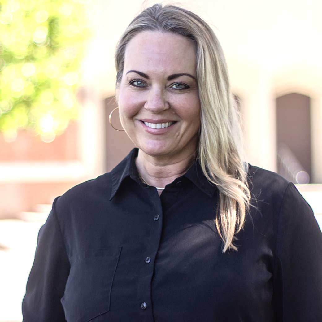 Woman with blonde hair wearing a black shirt, smiling, outdoors.