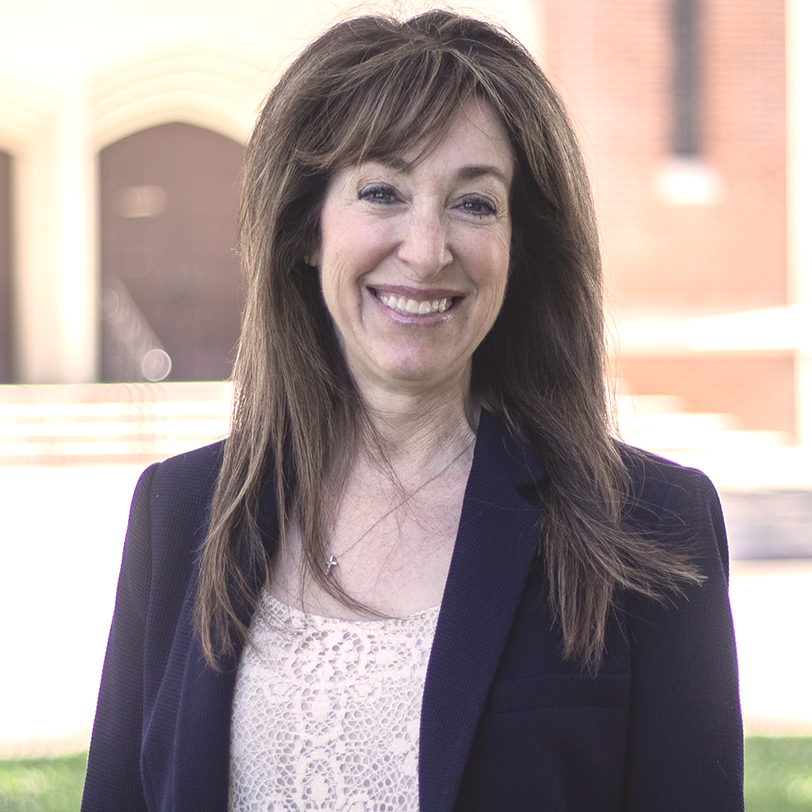 Woman smiling, wearing a navy blazer, standing outdoors in front of a building.